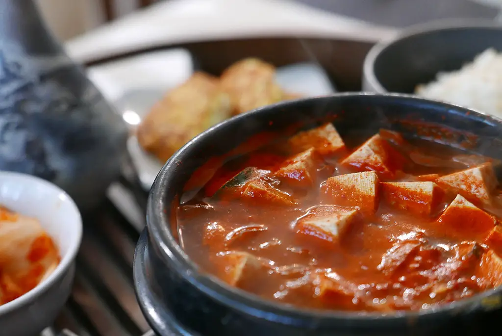 A closeup shot of Korean doenjang jjigae. The Korean stew is filled with tofu. 