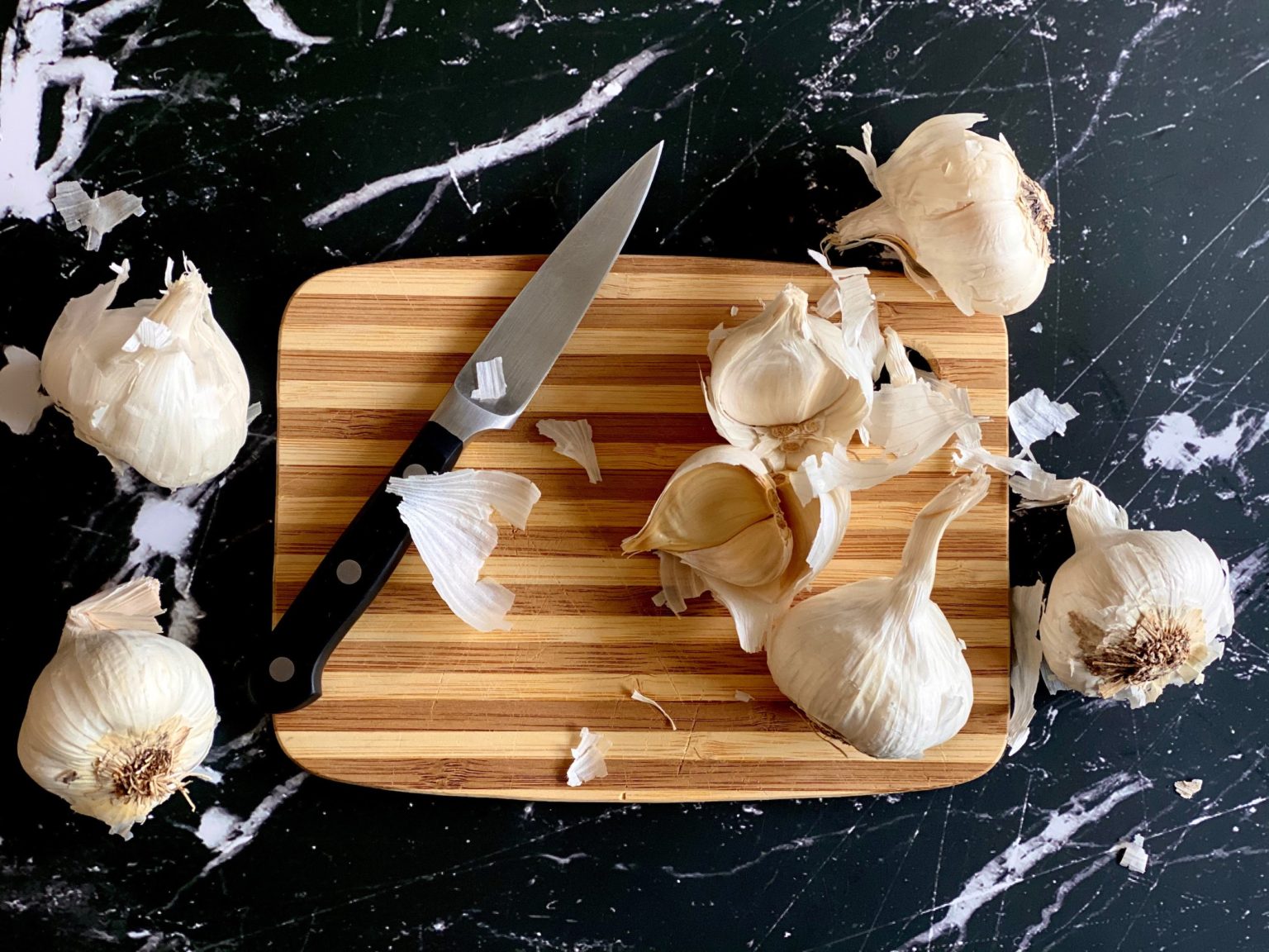 Our first of our kitchen tips and tricks is how to peel garlic easily. The photo is of garlic, and knife, and a cutting board. 