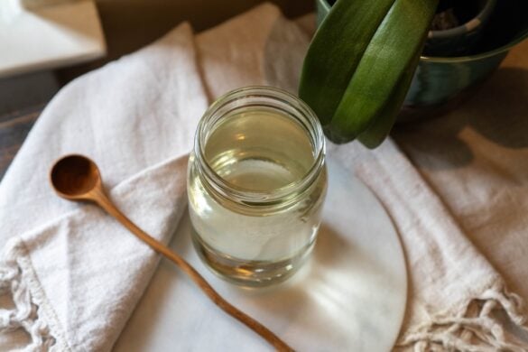An overhead shot of simple syrup in a mason jar. The jar sits on a marble circle topper next to a wooden spoon.