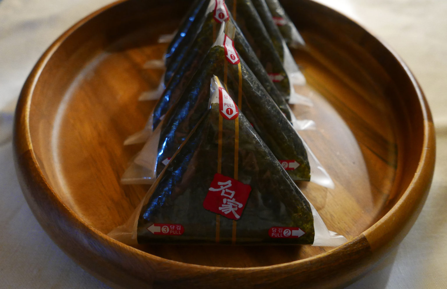 Triangle kimbap lined up on a wooden tray. 