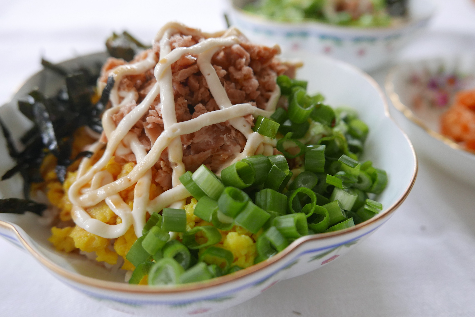 Tuna mayo rice--Rice topped with tuna, mayo, green onions, and seaweed strips, served in a floral bowl. 