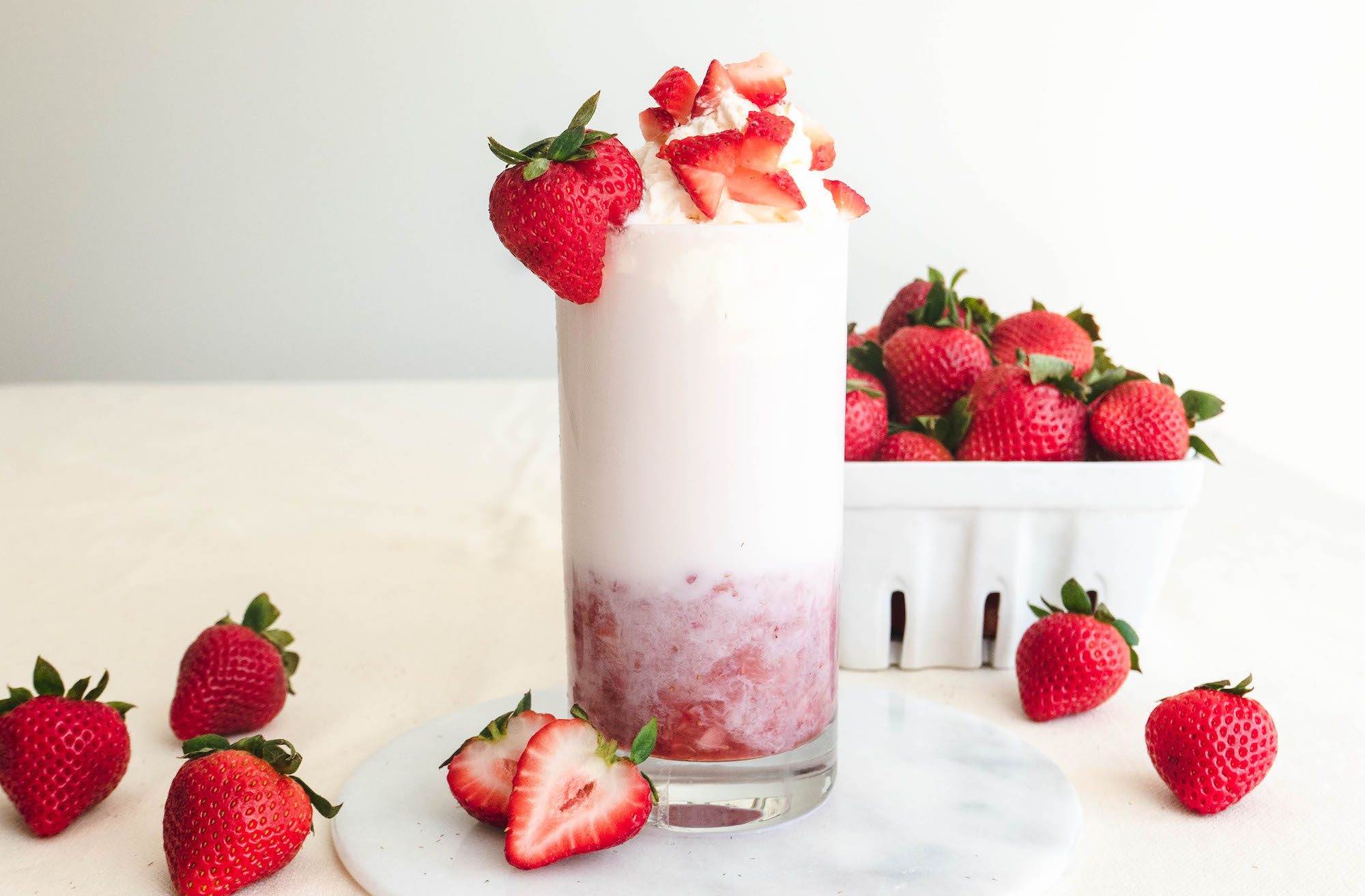 A tall glass of strawberry milk topped with whipped cream.