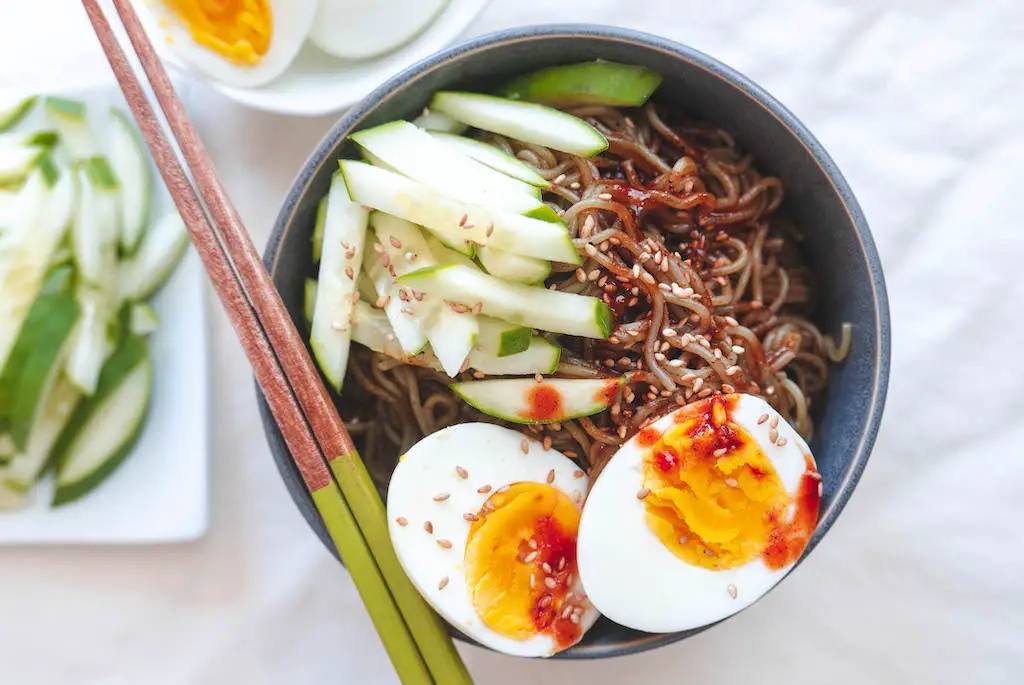 An overhead shot of spicy Korean cold noodles. Topped with boiled eggs and cucumbers