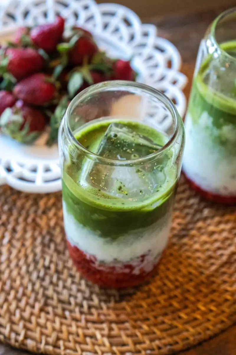 An overhead shot of strawberry matcha latte on a placemat. Strawberries sit on a white plate behind. 