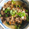 An over heat shot of a Korean grits bowl--grits topped with spinach, kimchi, ground pork, green onions, and sesame