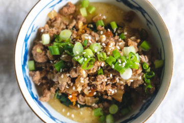 An over heat shot of a Korean grits bowl--grits topped with spinach, kimchi, ground pork, green onions, and sesame