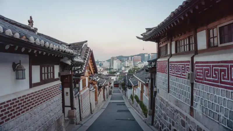 A traditional Korean street--a narrow road with old houses on the side. The houses are white with brown wood. The roofs are slate.