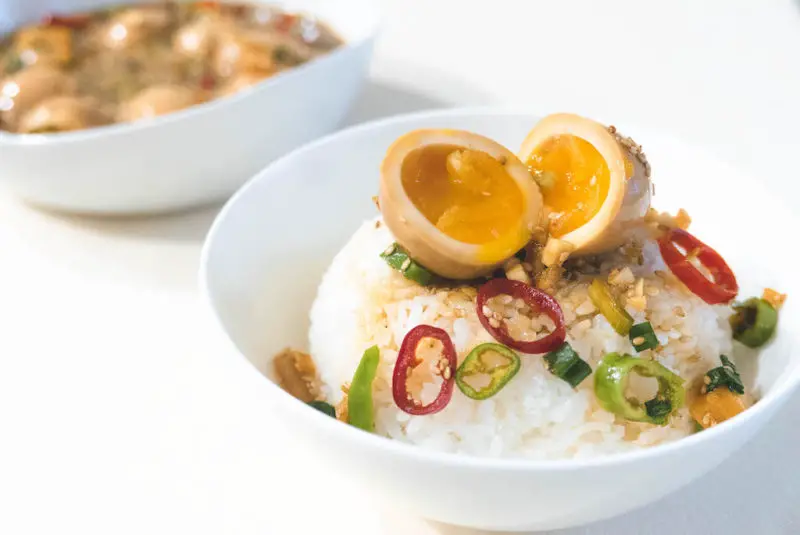 A bowl of white rice topped with a Korean mayak egg. The egg is cut in half and the jammy center is golden. Hot peppers also sit on the rice. 