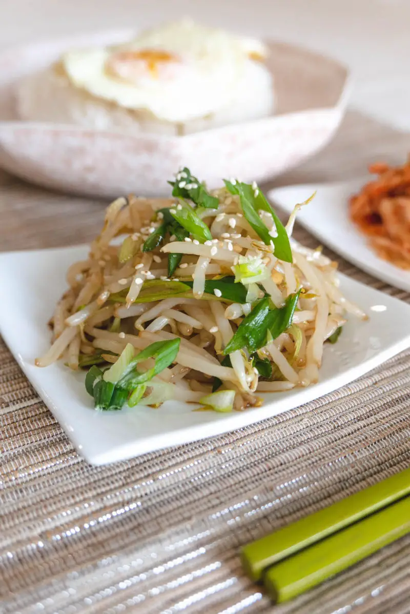 A side shot of Korean mung bean sprout salad next to a bow of rice with eggs. 