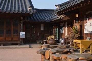 A shot of a traditional Korea building. The building has a black tile roof and dark wooden walls