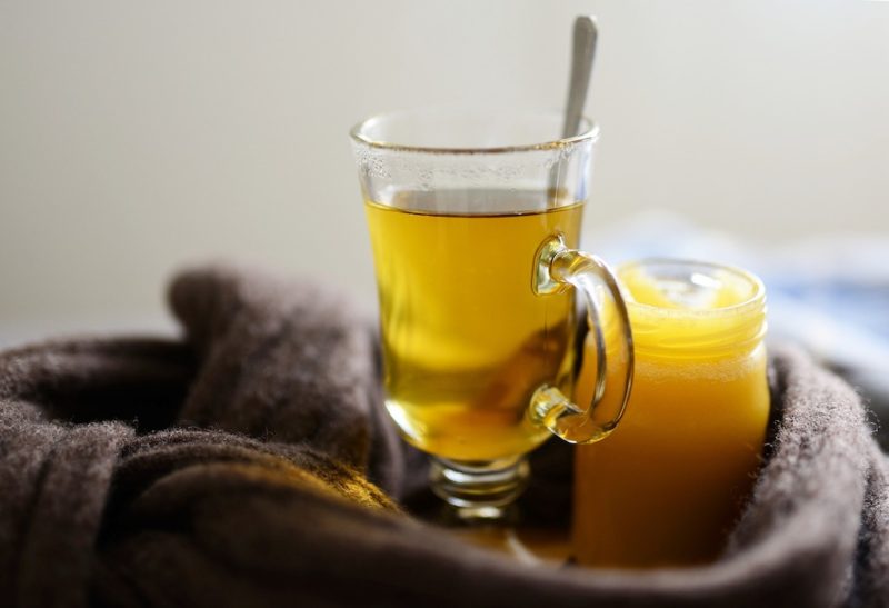 A hot glass of honey tea-- a jar of honey sits next to the glass of tea. 