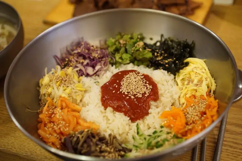 Bibimbap in a metal bowl. The bowl has rice, gochujang, soybean sprouts, radish, and more. 