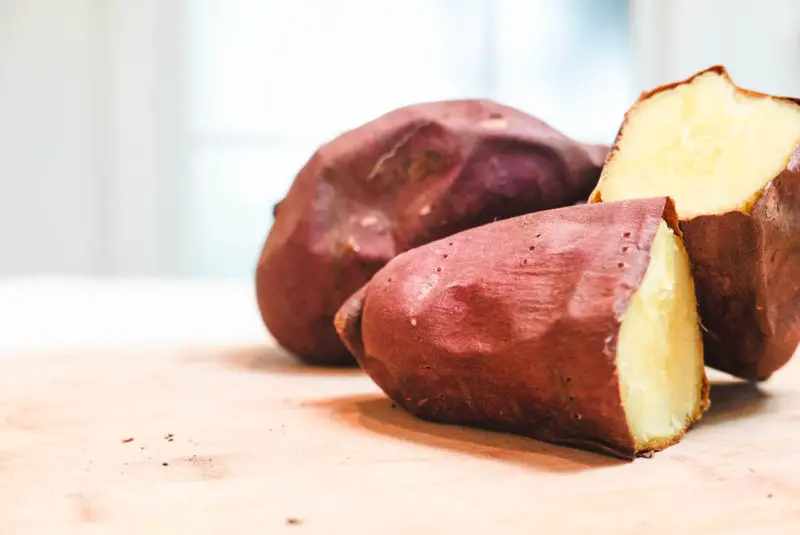 Korean sweet potatoes sliced in half on a wooden shopping block. 