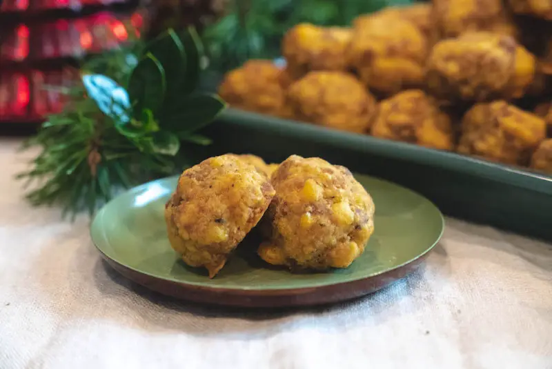 Vegetarian sausage balls on a small green plate. A pile on a platter sits behind. 