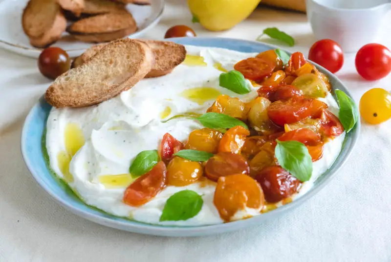 a plate of whipped feta. tomatoes and basil sit on top of the whipped feta. 