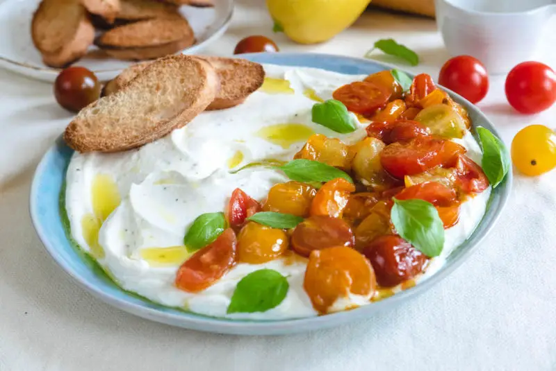 a plate of whipped feta. tomatoes and basil sit on top of the whipped feta.
