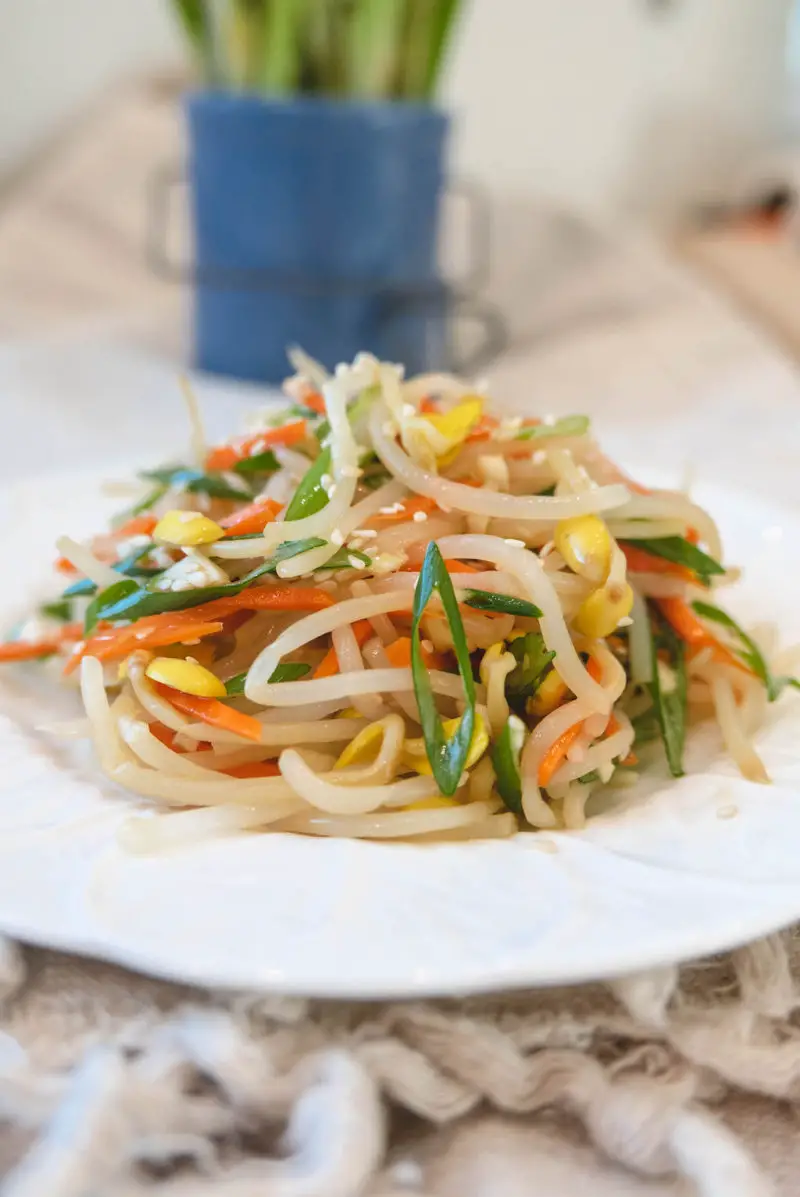 A closeup side shot of kongnamul muchim. This salad has green onions, carrots, and garlic mixed into the soybean sprouts. 