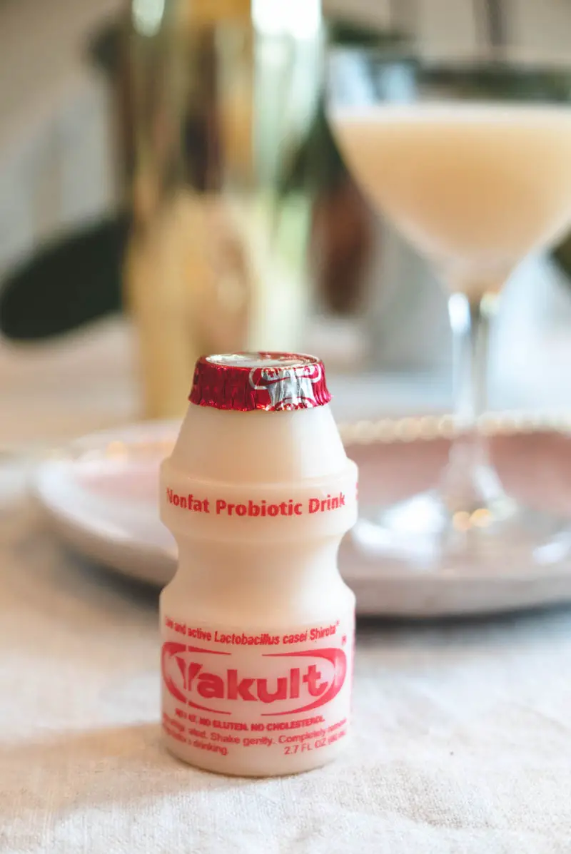 A closeup shot of a bottle of Yakult. The cocktail sits in the background.