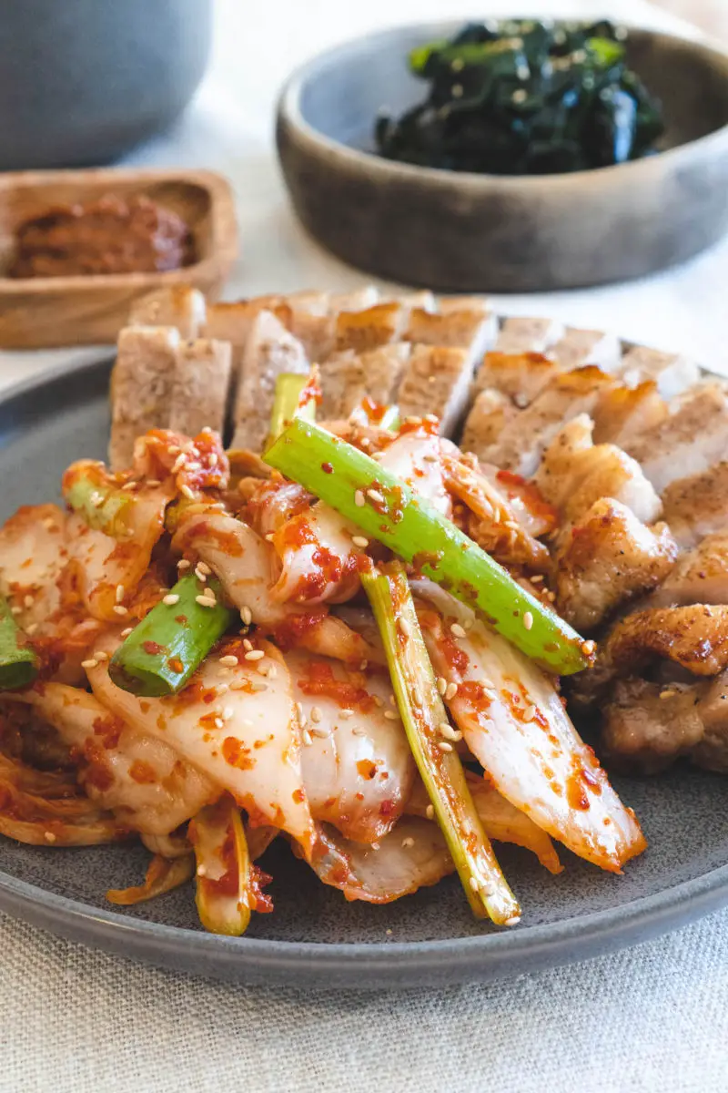 A plate of fresh kimchi with samgyeopsal. Further side dishes sit behind.