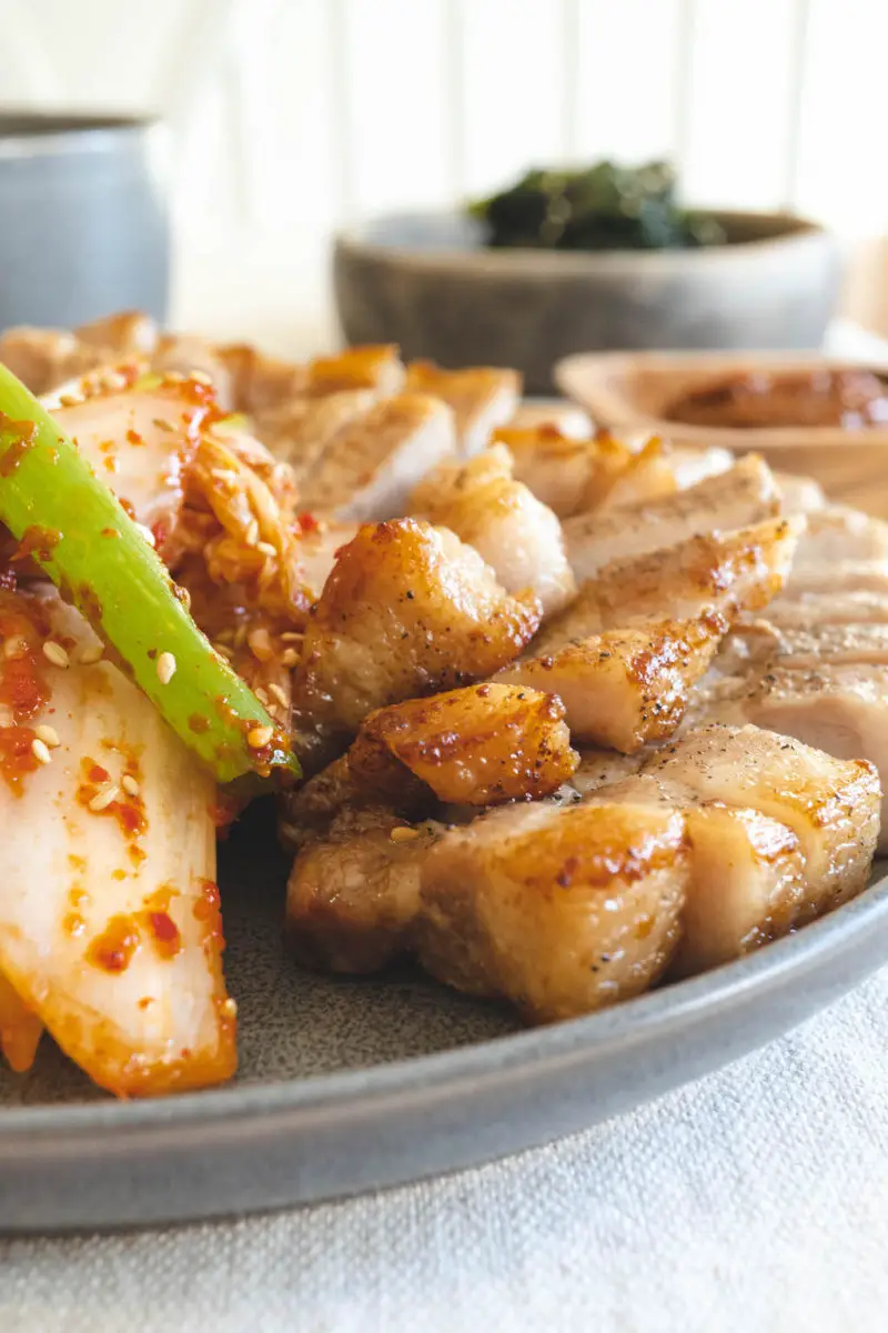 A side closeup shot of Korean barbecue. Baechu geotjeori sits next to the samgyeopsal.