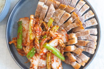 An overhead shot of fresh kimchi next to grilled pork belly