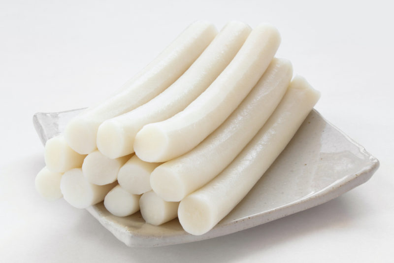 A side shot of Korean cylinder rice cakes stacked on a white square plate. 