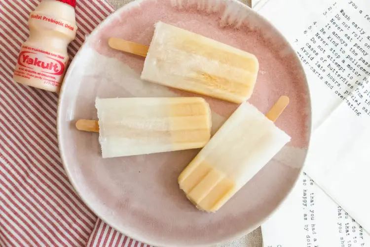 An overhead shot of Yakult soju popsicles on a pink plate. The plate sits next to a bottle of Yakult