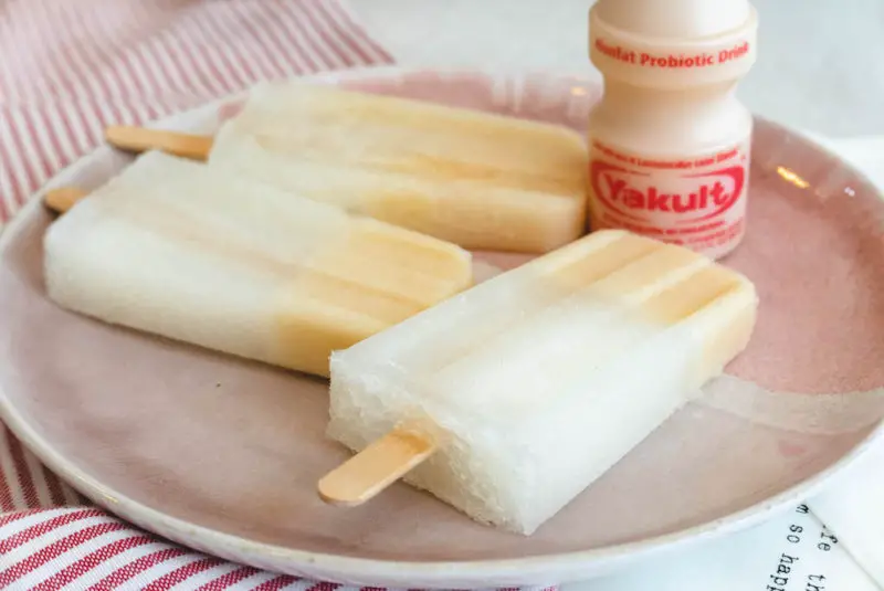 A side shot of Yakult soju popsicles next to a bottle of Yakult. 