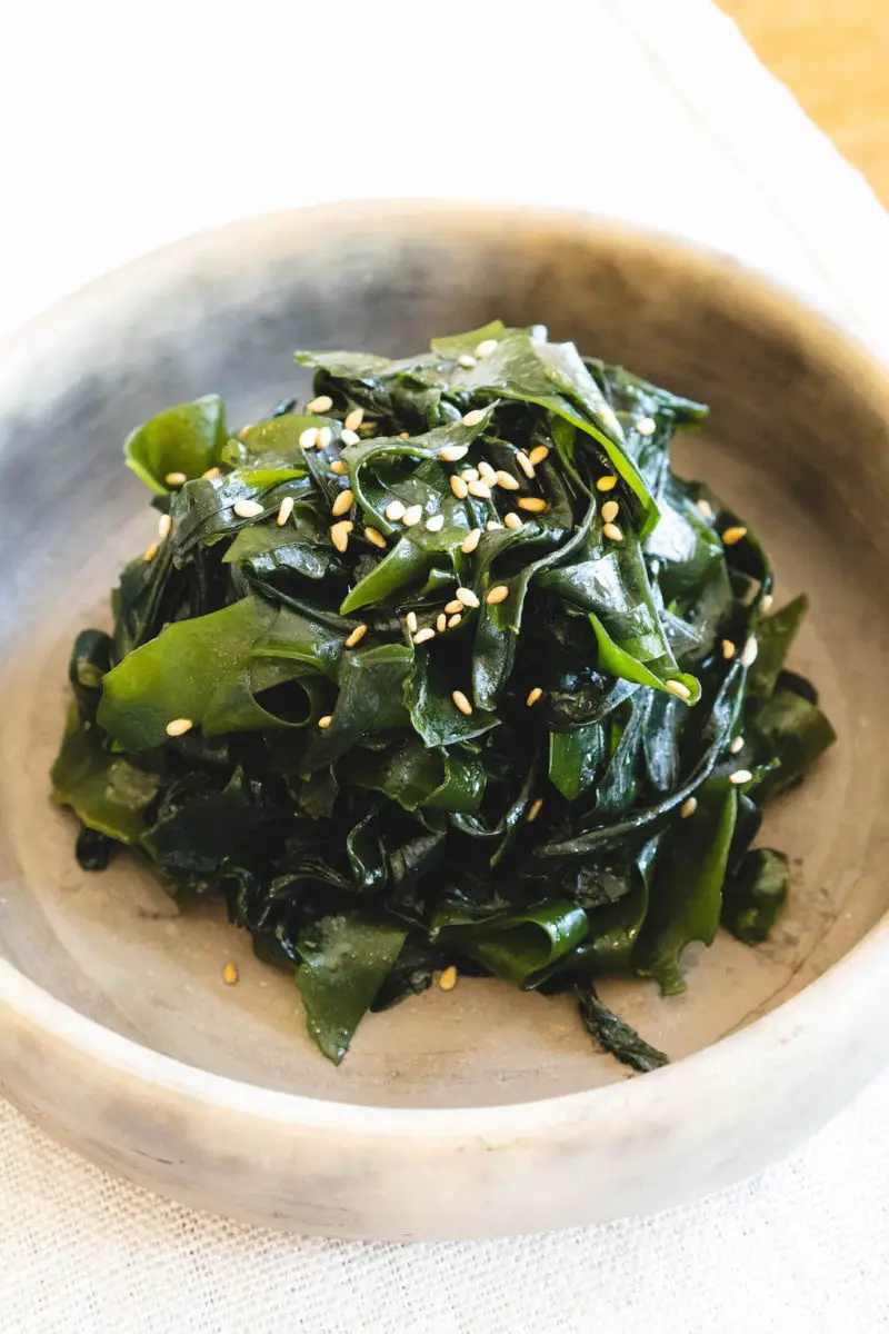 An overhead shot of bright green Korean seaweed salad. It sits in a stone bowl. 