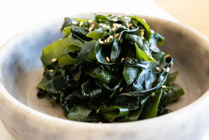 A side shot of Korean seaweed salad in a stone bowl. Sesame seeds it on top of the salad. 