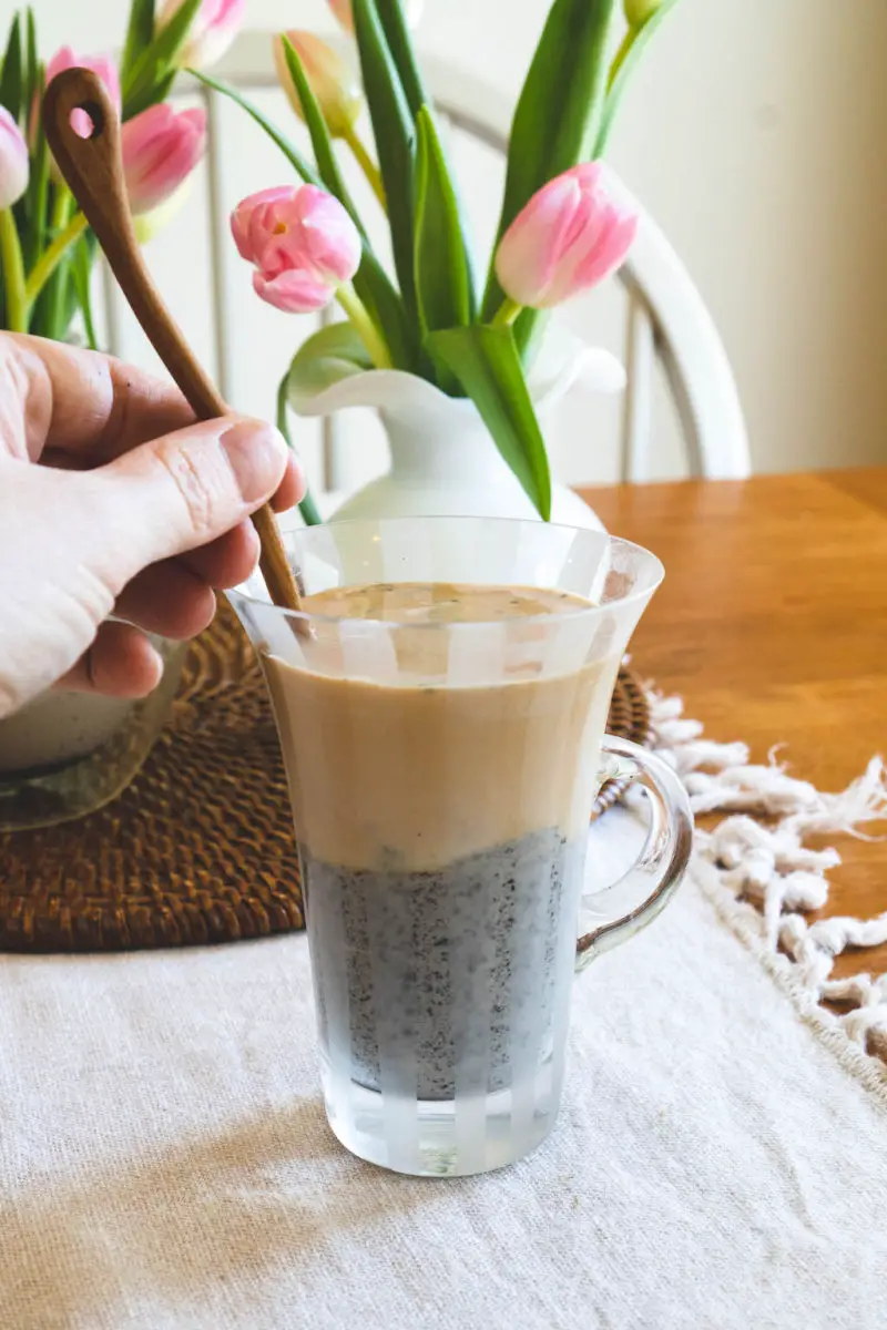 A cup of black sesame latte. In the cup is a wooden spoon and I am mixing the drink. 