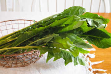 Fresh dandelion Greens in a copper wire bowl on the table.