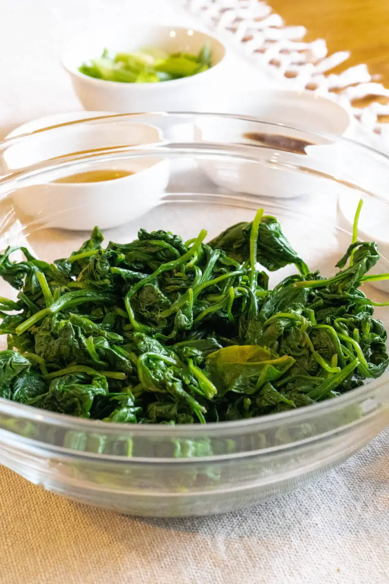 All the ingredients for Korean spinach salad behind a glass bowl filled with spinach.