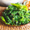 Korean spinach side dish on a wicker mat. Kimchi sits in the background.
