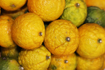A pile of yuzu fruit that is bright yellow and green.