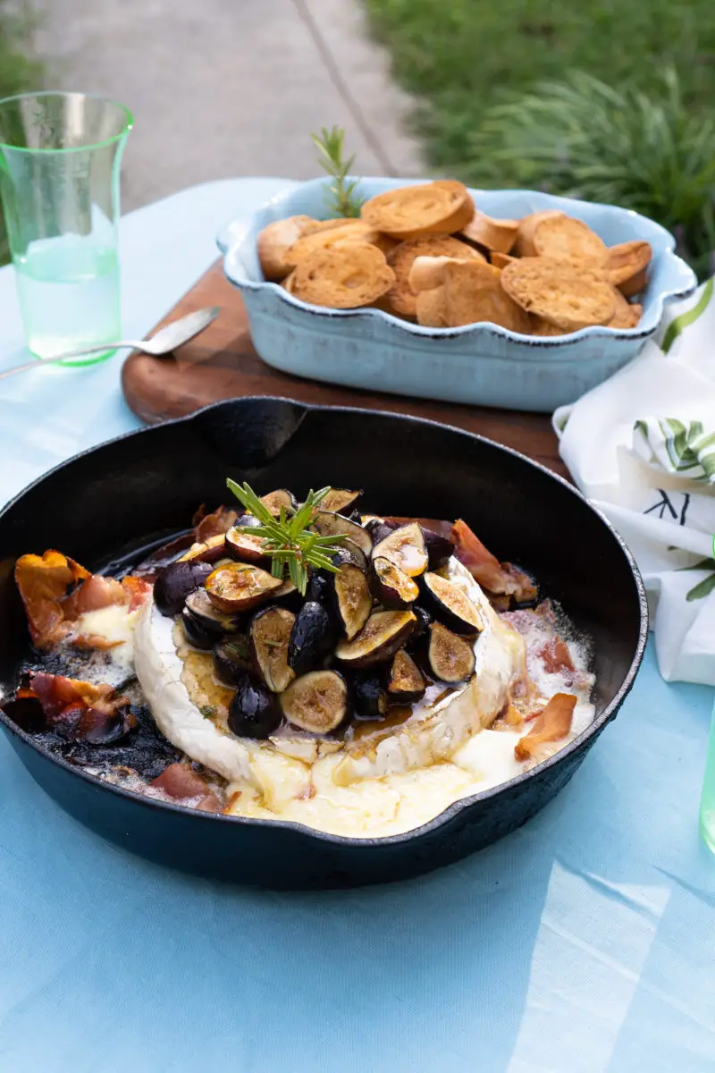 A side shot of brie topped with figs and rosemary in a cast iron skillet.