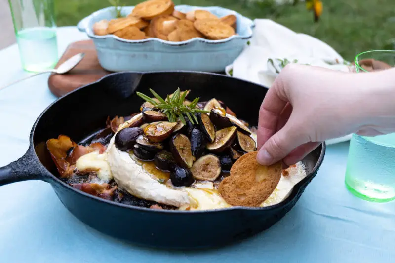 A photograph of a hang dipping toasted bread into the campfire brie.