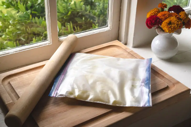 A bag of frozen milk and condensed milk on a cutting board next to a rolling pin. 
