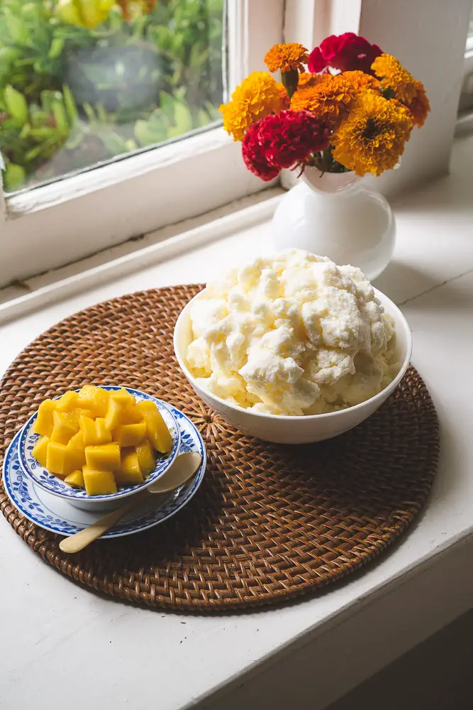 Shaved ice next to a bowl of cubed mango. 