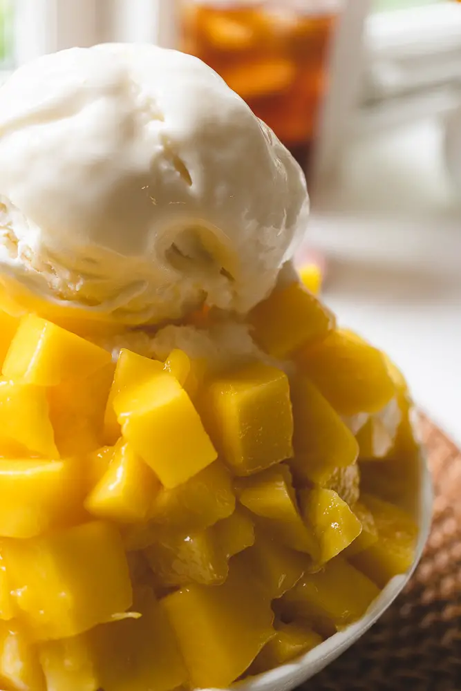 A closeup shot of mango sitting on the bingsu topped with vanilla ice cream.