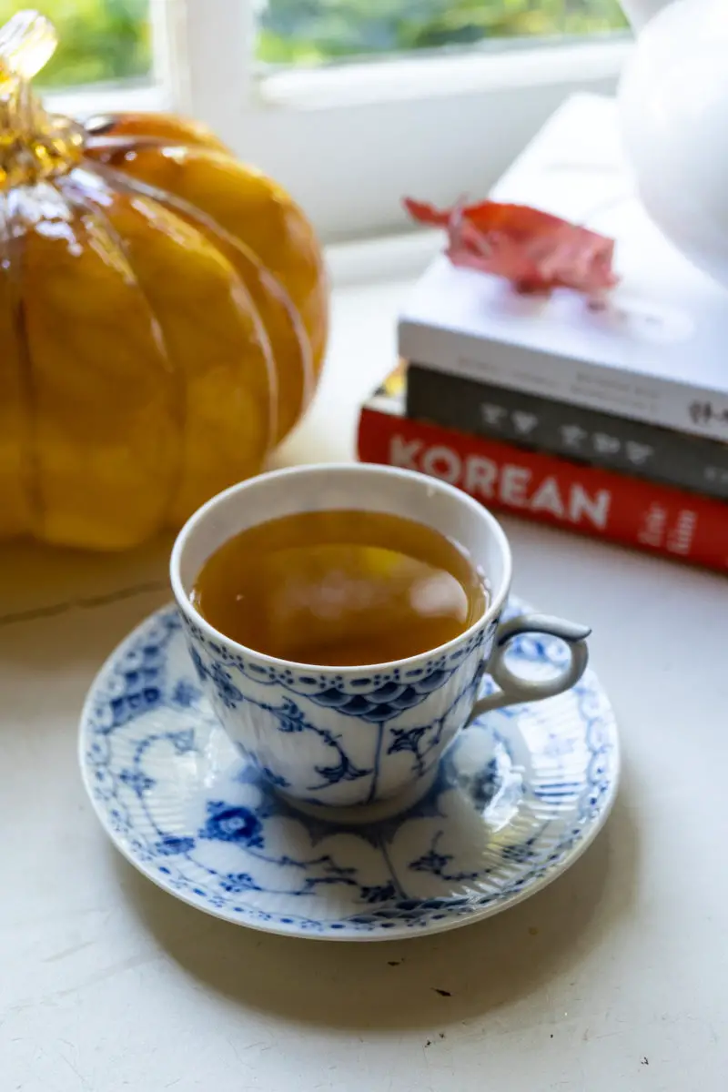 Maesil cha in a blue and white tea cup. Korean cookbooks and a glass pumpkin sits in the background.