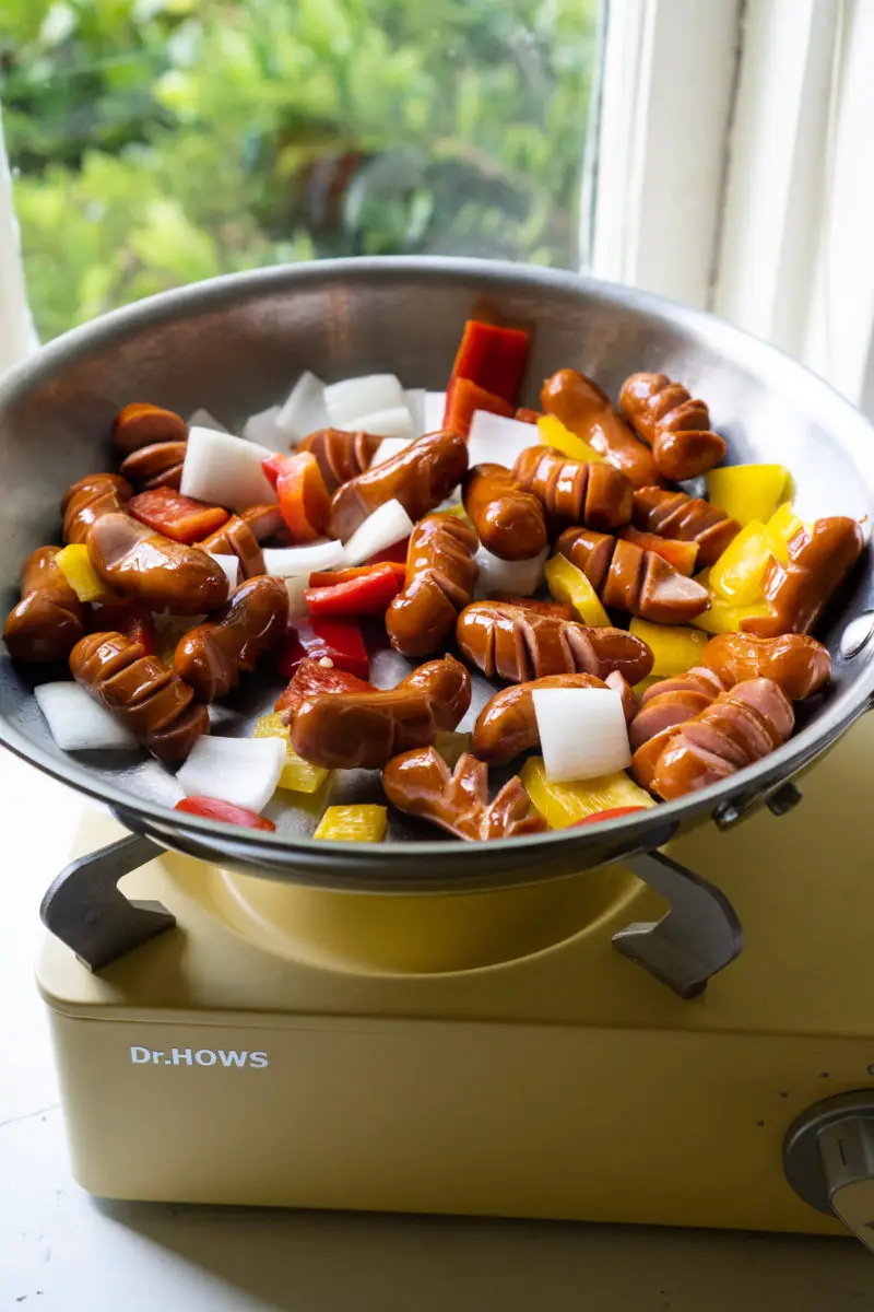 Sausage, onions, and peppers cooking on a yellow portable stovetop. 