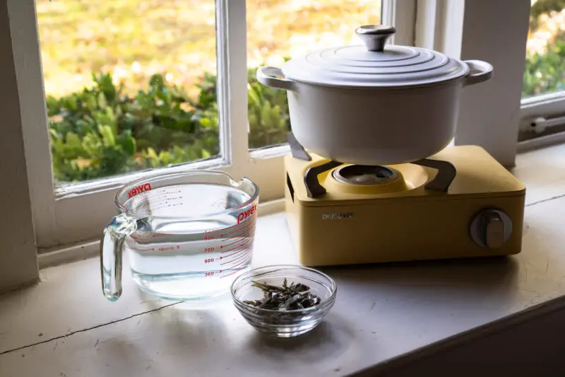 A side shot of the tools used to make myeolchi yuksu. A glass container filled with water, a bowl of dried anchovies, the yellow stovetop, and a pot.