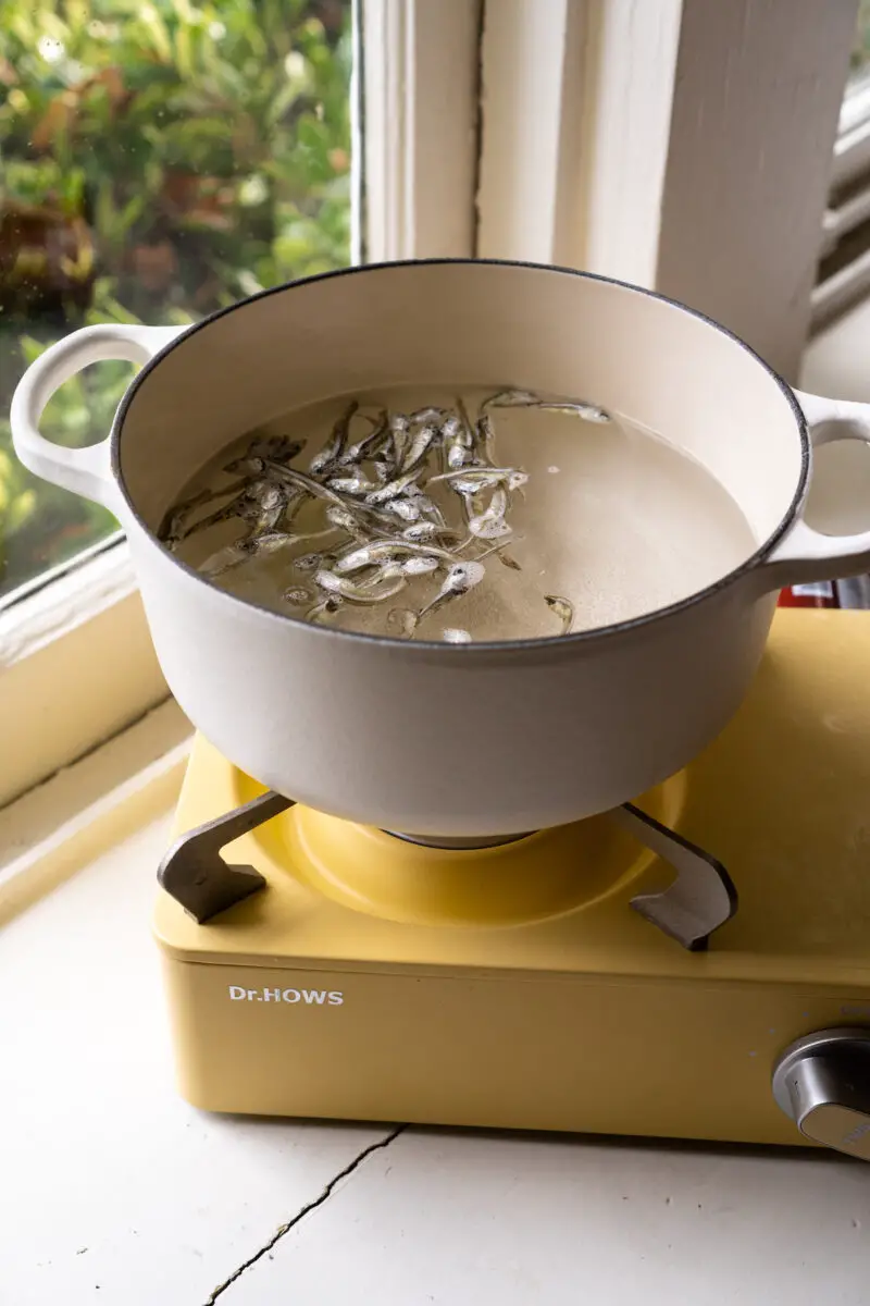 A white pot of dried anchovies boiling on a yellow stovetop.
