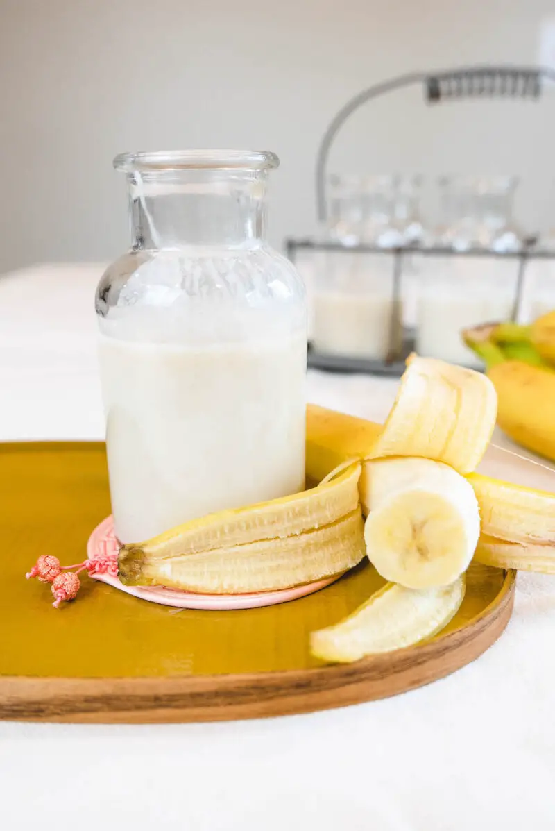 Korean banana milk in a jar on a yellow tray. The milk sits next to a peeled banana.