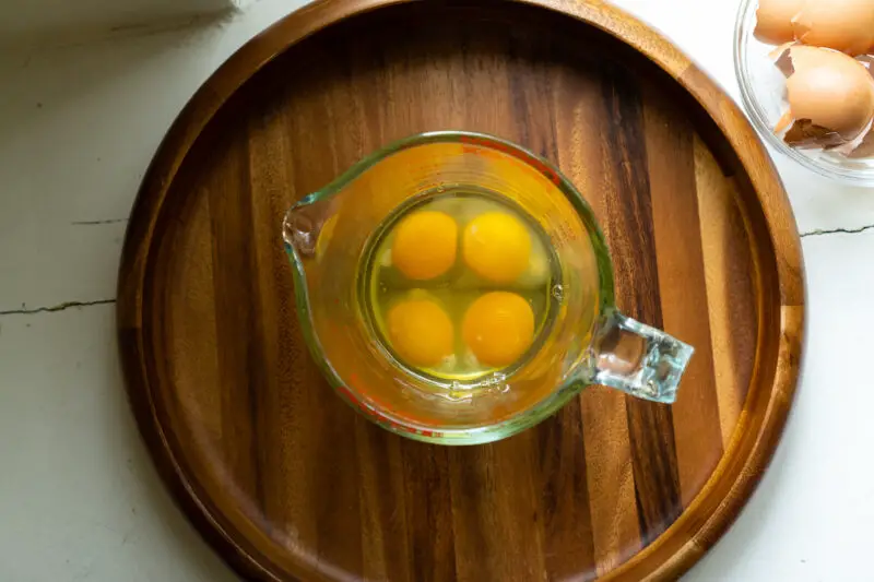 An overhead shot of four cracked eggs in a glass container.