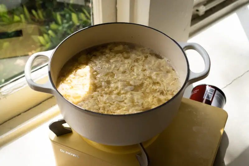 A side shot of Korean egg soup in a white pot on yellow cooktop. 