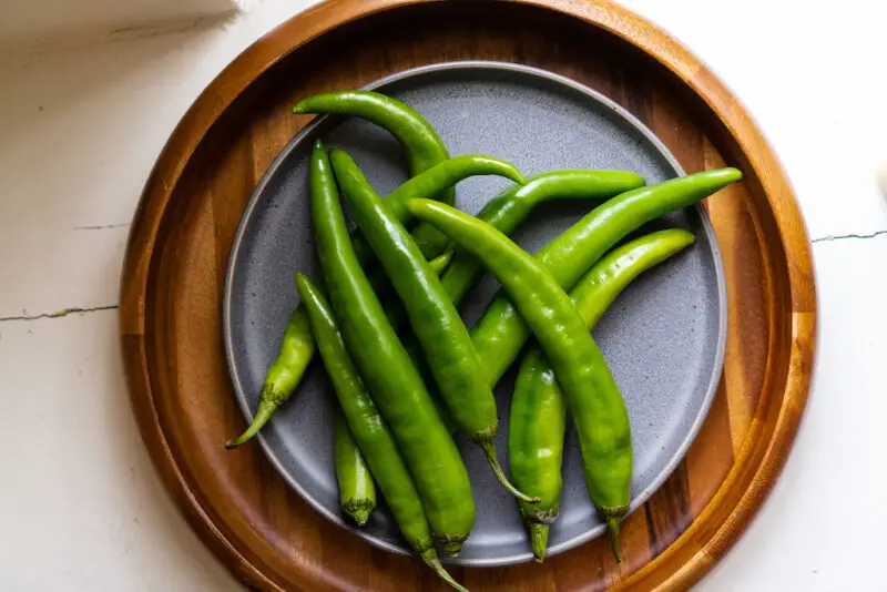 An overhead shot of Korean green peppers on a gray plate and wooden tray. 