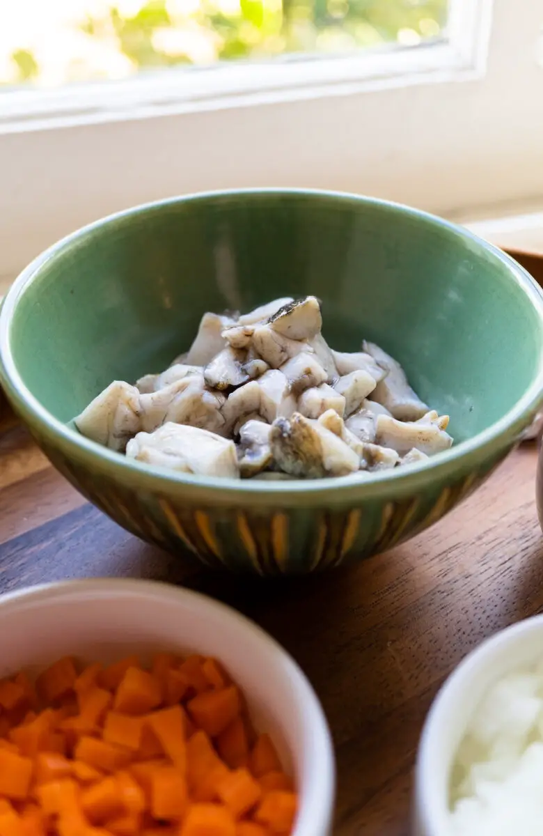 Chopped abalone sits in a green bowl. In the foreground sits minced carrots and onions in white bowls. 