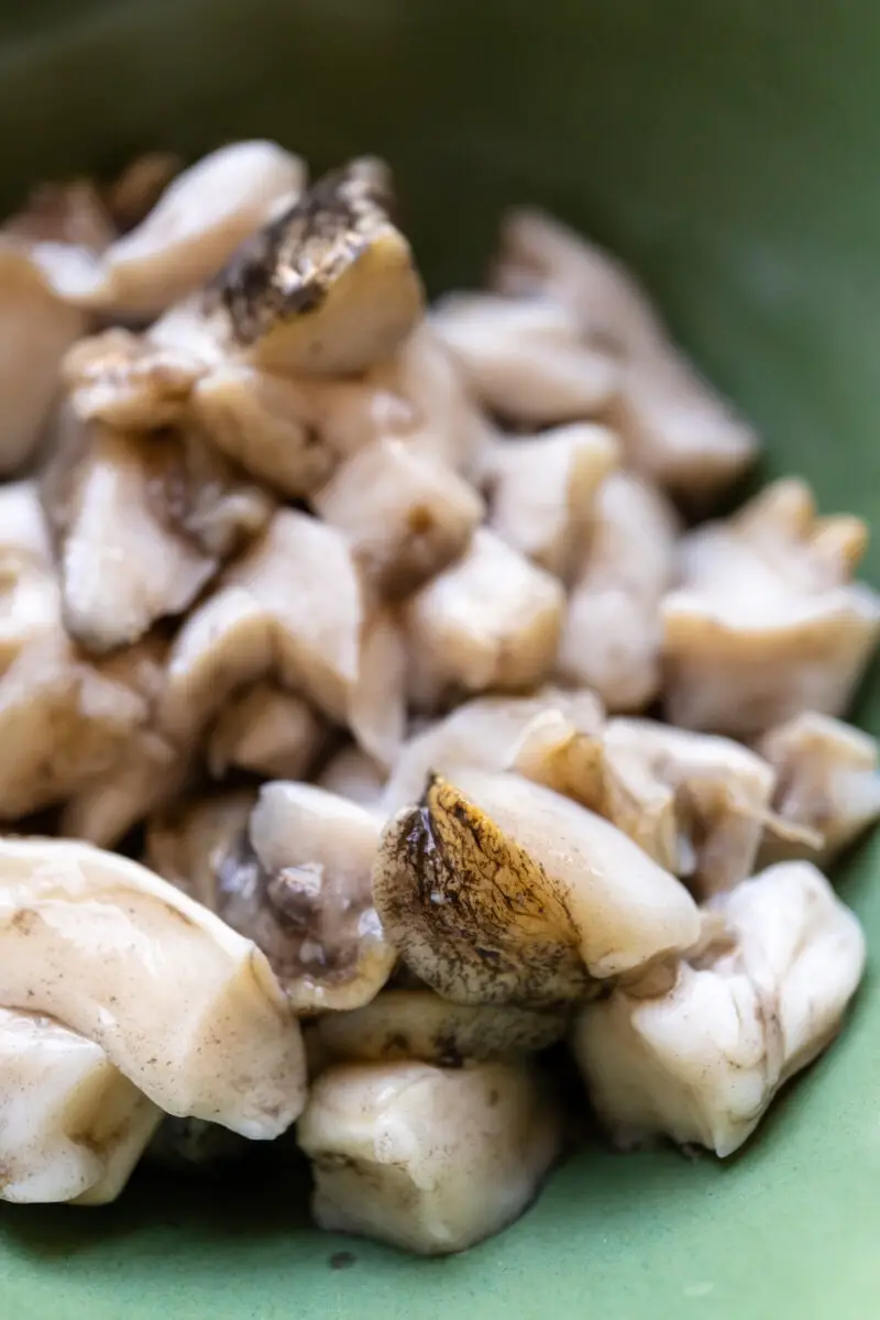 A closeup shot of abalone chopped into bite-sized pieces. They sit in a green bowl.